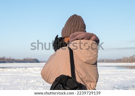A woman in winter clothes during a spring ice drift photographs the ice from the shore. Snowy cold northern landscape.