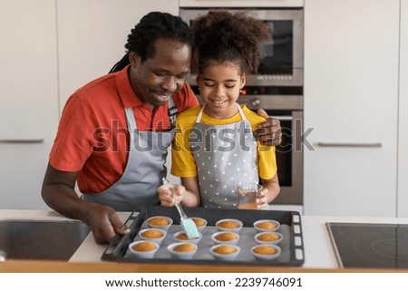 Cute Black Girl Brushing Egg Yolks On Muffins While Baking With Dad In Kitchen, Happy African American Father And Preteen Daughter Having Fun While Cooking Pastry Together At Home, Copy Space Royalty-Free Stock Photo #2239746091