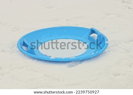 one round blue plastic sled plate lies on a snowdrift of white snow in the street