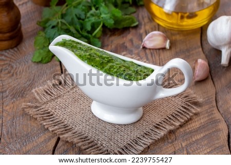 Green, spicy Cilantro Sauce with garlic and olive oil served in white ceramic sauce boat with ingredients. Selective focus, horizontal, wooden table. Royalty-Free Stock Photo #2239755427
