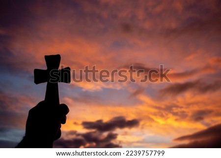 A hand holds a cross in backlight at sunrise. selective focus. copy space