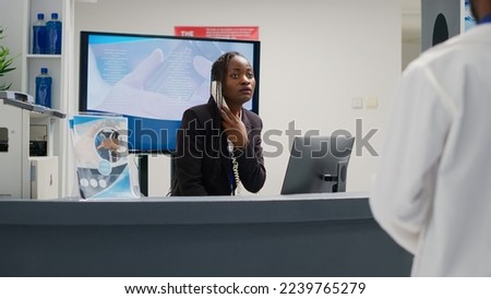 African american woman answering landline phone call at reception counter, working in hospital to give support to patients. Young adult uing telephone with cord at health center front desk. Royalty-Free Stock Photo #2239765279