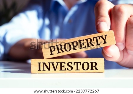 Closeup on businessman holding a wooden blocks with text PROPERTY INVESTOR, business concept