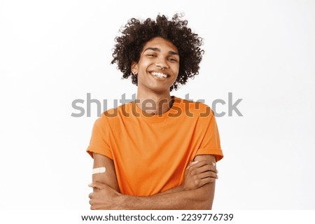 Portrait of smiling queer guy with vaccine shot, patch on arm from vaccination, covid-19 pandemic concept, standing over white background