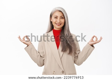 Keep calm. Asian senior woman in business suit, meditating, deep breath, inhale air and relaxing, standing over white background