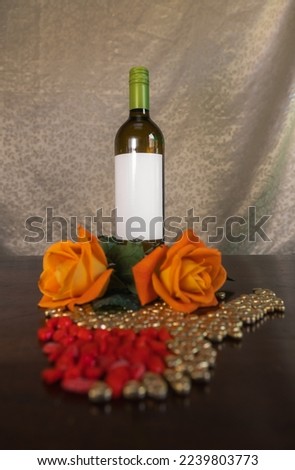 Bottle of wine next to orange roses and red and gold heart-shaped chocolates on indoor table
