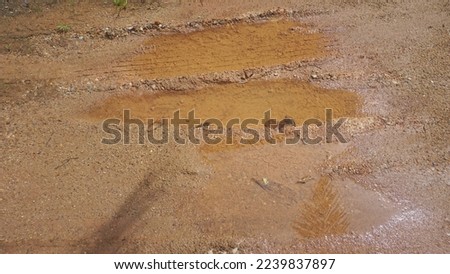 Tire tread prints on muddy soil. Wheel tyre track marks on wet ground. Puddle of rain water and tire tracks on muddy dirt road Royalty-Free Stock Photo #2239837897