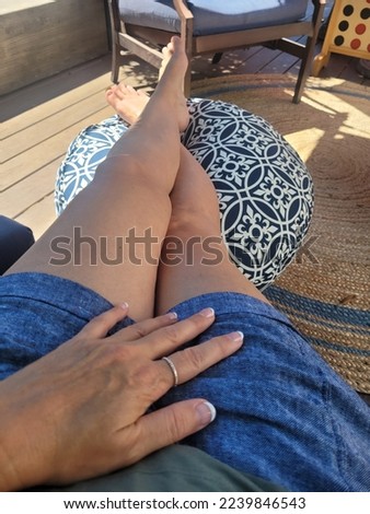 lady woman relaxing on the deck patio in the garden on sunny day while in the shade with her legs up in shorts barefoot