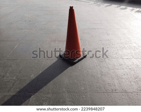 Orange traffic cone and its shadow on pavement floor.