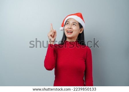 Pretty lovely lady asian thai women in red sweater and santa christmas hat isolated over grey background. pointing