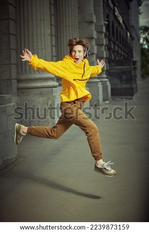 Happiness. Carefree boy teenager jumping for joy on a city street and listens to music in headphones. Summer, active lifestyle. 