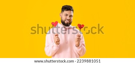 Young man with red paper hearts on yellow background