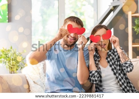 Funny lovely couple with red paper hearts at home