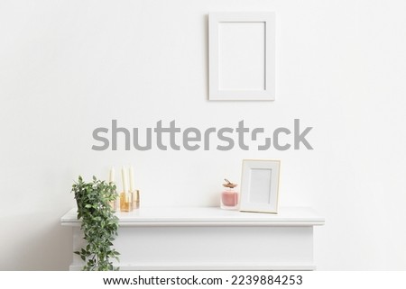 Blank photo frame, candles and houseplant on mantelpiece near white wall