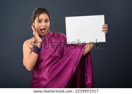 A young girl or woman wearing an Indian traditional saree holding a signboard in her hands on gray background.