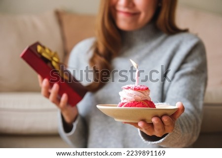Closeup image of a young woman holding and giving a gift box and birthday cake with candle