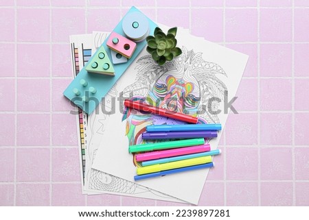 Coloring pages, felt-tip pens, educational blocks and flowerpot on pink tile background