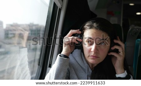 Woman wearing headphones while commuting by train. Female passenger puts noise cancelling headphone listening to music podcast or audiobook