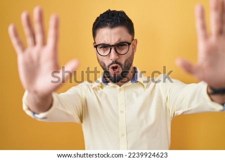 Hispanic young man wearing business clothes and glasses doing stop gesture with hands palms, angry and frustration expression 