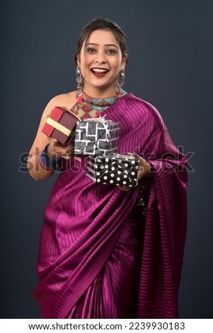 Portrait of a young happy smiling woman wearing a saree holding gift box on a grey background.