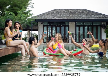Group of diverse friend jumping into the pool, having a party together. Attractive young man and woman hanging out, celebrating summer vacation enjoying sunny day on travel holiday at a private villa.