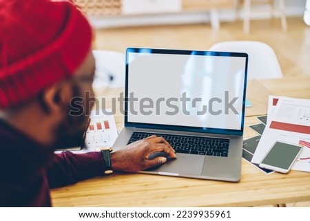 From above back view of crop African American male entrepreneur sitting at table in contemporary workspace and browsing netbook while working on project