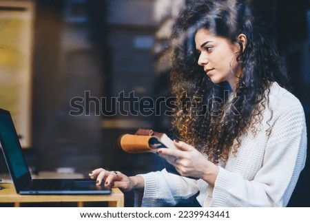Skilled female student with education textbook watching informative webinar via laptop application, side view of millennial hipster girl with notepad using netbook for reading knowledge publication