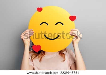 Emoticon in love. Girl holds a yellow smiley with romantic love face emoticon isolated on a grey background. Valentine's day concept Royalty-Free Stock Photo #2239945731