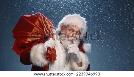 close up portrait of the good old Santa Claus secret hand and lips with a bag of gifts under a snowfall on a red background. Merry Christmas and Happy New Year. Secret Santa