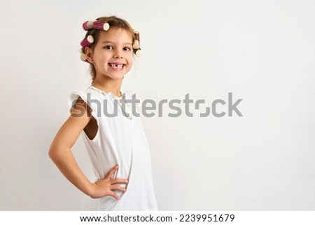 Little girl with curlers on white background with copy space. Close-up portrait of a child girl with hair curlers. Kids beauty and fashion