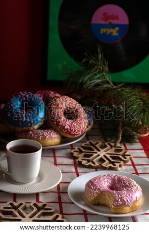 photo multicolored doughnuts lying in a plate and a cup of coffee on a saucer standing on the table next to wooden snowflakes