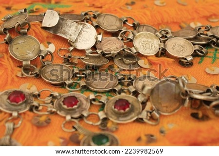An artistic painting made by Moroccan, Amazigh, Susian hands. It is a necklace made of the old silver Moroccan dirham coin, and under it is a handmade loincloth with ancient Moroccan colors.