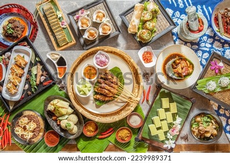 Tasty looking Thailand food served on the table with a variety of chili sauces,Curry Beef Skewers,coconut milk jelly, rice, prawns, chicken and spring roll. south east Asia food.top view Royalty-Free Stock Photo #2239989371