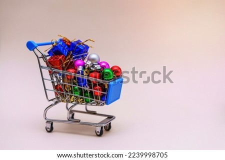 Christmas new year shopping mock up with trolley, gifts and decorations on christmas tree, balls of different colors on light pink background. Minimal winter december sale or shopping mall concept.