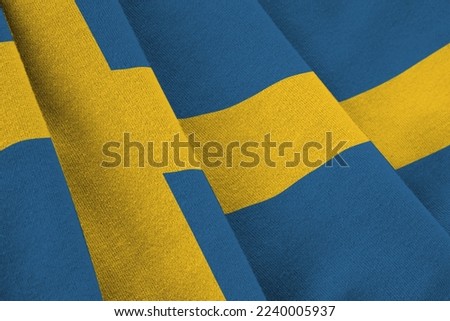 Sweden flag with big folds waving close up under the studio light indoors. The official symbols and colors in fabric banner