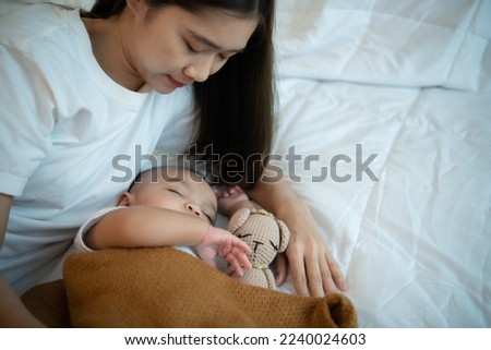 Young mother hugging her newborn child to lull the baby to sleep in the white bedroom, warm sunlight in the evening of the day.