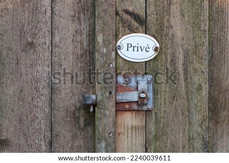 Closeup of old weathered wooden fence door with rusty metal lock handle and white oval private property sign with text privé in dutch.