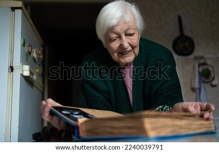 Cheerful senior female holding family photo album sitting at home. nostalgia concept and memory of old times. 