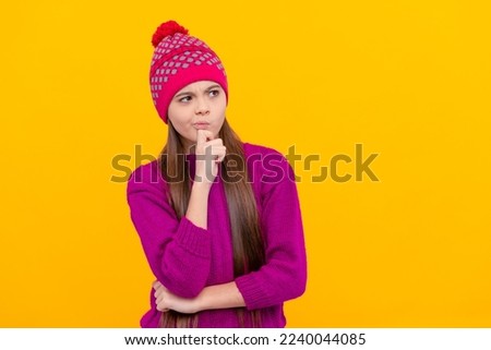 pondering child in winter hat on yellow background, winter clothing