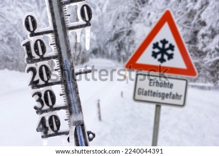 thermometer shows cold temperature at winter day and warning sign in german language: increased danger of black ice