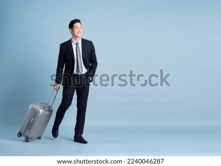 Portrait of Asian businessman wearing a suit and pulling a suitcase Royalty-Free Stock Photo #2240046287
