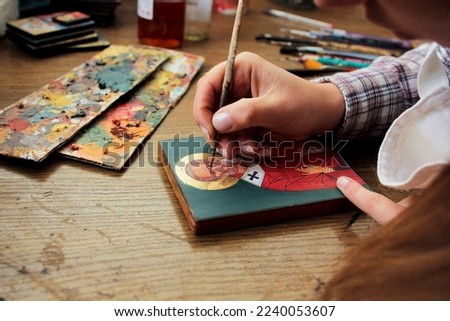 Artist paints a picture of acrylic paints. Close-up view. Artist's desktop.Reproduction of the icon of St. Nicholas. Workflow of the artist in the studio. Brushes and paints on the background art work Royalty-Free Stock Photo #2240053607