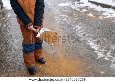 Child scattering gravel sand on footpath to reduce slipperiness. Royalty-Free Stock Photo #2240067259