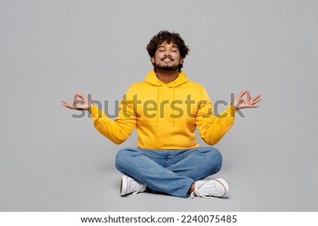 Full body spiritual young Indian man 20s he wear casual yellow hoody sit hold spreading hands in yoga om aum gesture relax meditate try to calm down isolated on plain grey background studio portrait Royalty-Free Stock Photo #2240075485