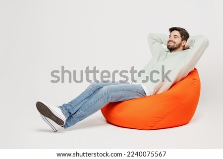 Full body young minded dreamful happy smiling man wear mint hoody sit in bag chair look camera hold hands behind neck isolated on plain solid white background studio portrait People lifestyle concept