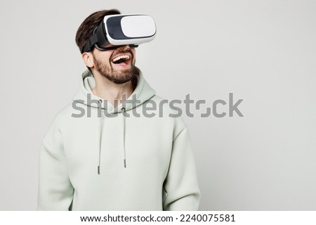 Young smiling amazed happy fun cheerful gambling caucasian man wearing mint hoody watching in vr headset pc gadget isolated on plain solid white background studio portrait. People lifestyle concept