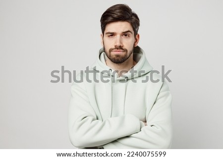 Young displeased sad caucasian man wear mint hoody look camera holding hands crossed folded waiting for apologises isolated on plain solid white background studio portrait. People lifestyle concept