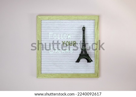 Expression - Follow your dreams - written from white and golden letters on letter board. Eiffel tower souvenir. Pink background. Top view. Copy space. Selective focus.