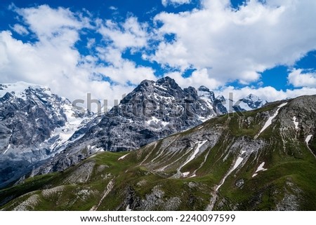 Passing clouds over idyllic landscape in the Alps with snow-capped mountain tops in the background. Alpine mountains ridge landscape in the beauty of the French, Italian and Swiss Alps. Royalty-Free Stock Photo #2240097599