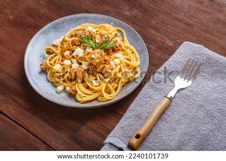 Homemade bolognese pasta on a plate next to a checkered napkin and a fork. Horizontal photo